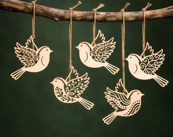 May include: Five wooden bird ornaments hanging from a branch with twine. Each bird has a unique openwork design on its wings and tail. The birds are light-colored against a dark green background, creating a natural, rustic aesthetic.