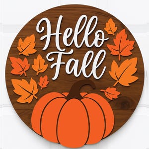 May include: A round wooden sign with the words "Hello Fall" in white script. The sign features an orange pumpkin and orange fall leaves. The background is a dark brown wood grain.
