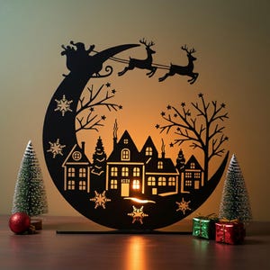 May include: A black metal Christmas decoration featuring a silhouette of Santa Claus in a sleigh pulled by reindeer over a town. The design includes snowflakes, trees, and houses. Two small Christmas trees and gifts are on the sides.