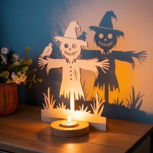 May include: Wooden scarecrow tea light holder with a bird perched on its arm. The scarecrow has a hat and a stitched smile. The candle holder is on a wooden base, casting a shadow of the scarecrow on the wall. A decorative item for Halloween.