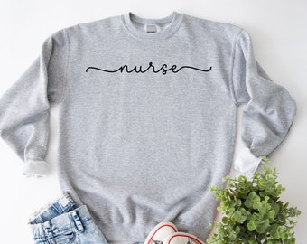 Puede incluir: Sudadera gris con la palabra "nurse" escrita en cursiva en la parte delantera.
