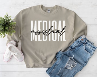 May include: A light brown sweatshirt with the text "MEDICAL assistant" printed in white letters with a black outline.