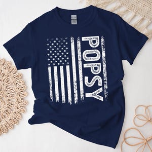 May include: Navy blue t-shirt with a white distressed American flag and the word "POPSY" printed on it.