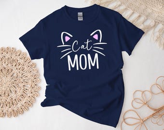 Peut inclure: Un t-shirt bleu marine avec un visage de chat blanc et le texte "Cat Mom" en blanc.