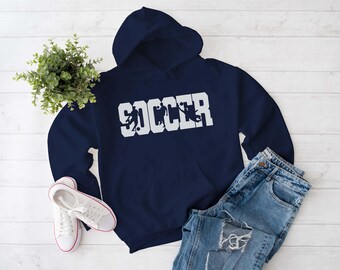 May include: A navy blue hoodie with a white graphic of football players and the word "SOCCER" printed on the front.