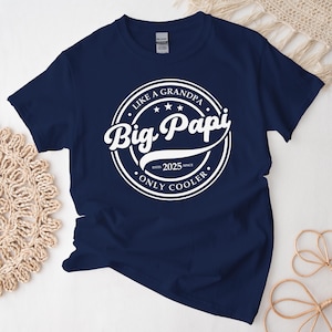 May include: Navy blue t-shirt with a white circular graphic that reads "Like a Grandpa Big Papi Only Cooler estd 2025". The shirt is made of a soft material and has a crew neck.