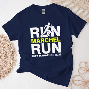 Puede incluir: Camiseta azul marino con las palabras "RUN MARCHEL RUN" en blanco y amarillo, junto con la silueta de un corredor. El texto "CITY MARATHON 2025" está impreso debajo de la palabra "RUN".
