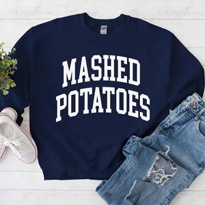 May include: A navy blue sweatshirt with the text "MASHED POTATOES" in white letters.