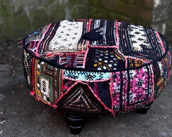 Puede incluir: Un puf redondo de patchwork multicolor con patas negras. El puf está hecho de varias telas con diferentes patrones y texturas, incluyendo diseños florales, geométricos y paisley.