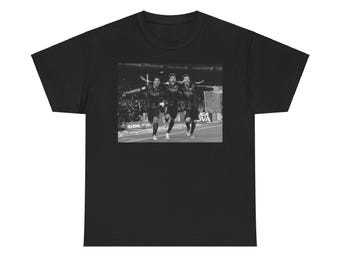 May include: Black t-shirt featuring a grayscale image of three soccer players celebrating a goal. The players are wearing dark jerseys with sponsor logos. The background shows a stadium with spectators.