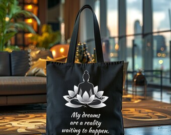 May include: Black tote bag featuring a white and gray illustration of a meditating figure in a lotus position, with the text "My dreams are a reality waiting to happen." The bag has long black handles.