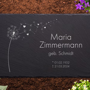 Könnte beinhalten: Schwarze Schiefer-Gedenktafel mit einem weißen Löwenzahnmuster und dem Text "Maria Zimmermann geb. Schmidt * 01.02.1952 † 21.03.2024"