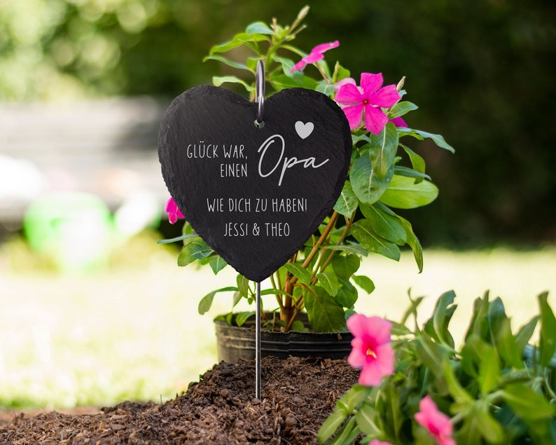 K&ouml;nnte beinhalten: Ein schwarzer herzf&ouml;rmiger Schiefer-Gartenmarker mit dem Text "Gl&uuml;ck war einen Opa wie dich zu habeni Jessi & Theo" und einem kleinen wei&szlig;en Herz.