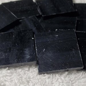 May include: A pile of black square mosaic tiles. The tiles are smooth and have a slight sheen.
