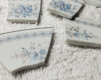 May include: A collection of broken porcelain pieces with a blue and white floral pattern. The pieces are arranged on a white fluffy surface.