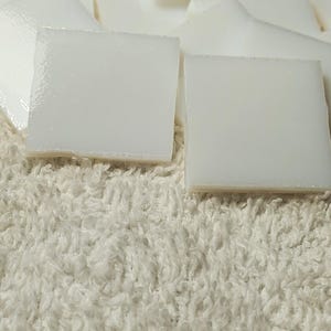 May include: A pile of white ceramic tiles, some are stacked on top of each other, on a white fluffy surface.