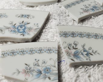May include: Close-up of broken pieces of a white ceramic plate with a blue and gold floral pattern. The plate is decorated with a delicate floral design featuring blue flowers and gold accents. The text "Spode China Christine Japan" is visible on one of the pieces.
