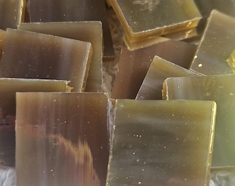 May include: A collection of small, square, translucent tiles in shades of brown and yellow. The tiles are scattered on a white, textured surface, creating a mosaic effect. The tiles have a slightly iridescent quality.