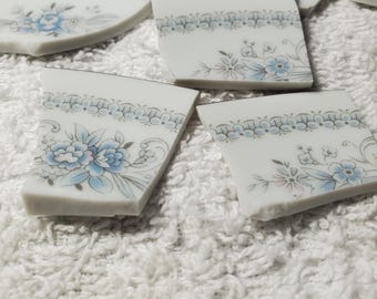 May include: Five broken pieces of a white ceramic teacup with a blue floral pattern. The pieces are on a white fluffy surface. The text "Christine Japan" is visible on one of the pieces.