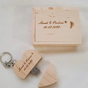 Peut inclure: Une clé USB en bois en forme de cœur avec un porte-clés, gravée avec "Sarah & Orelois 18.03.2023" et un petit cœur. La clé USB est ouverte, révélant le port USB. La clé USB est dans une boîte en bois avec la même gravure.