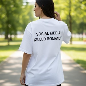 Op de afbeelding: Wit T-shirt met de tekst "SOCIAL MEDIA KILLED ROMANCE" in het zwart gedrukt. Het shirt heeft een klassieke ronde hals en korte mouwen. De afbeelding toont de achterkant van het shirt.
