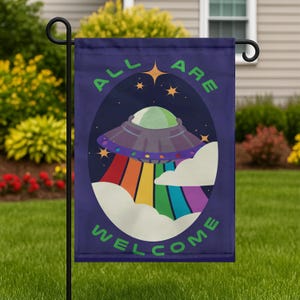 May include: A dark blue garden flag with the words "ALL ARE WELCOME" in green. The flag features a cartoon image of a UFO with a rainbow beam and clouds. The UFO is purple, green, and gray.