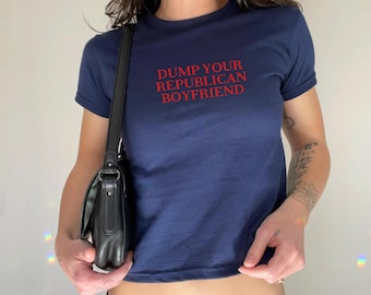 May include: Navy blue crop top with the text "DUMP YOUR REPUBLICAN BOYFRIEND" in red. The t-shirt has short sleeves and a crew neck. A black shoulder bag is visible.