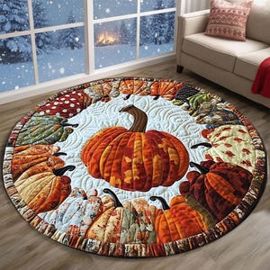 May include: A round, quilted rug featuring a large orange pumpkin in the center, surrounded by a ring of smaller pumpkins in various colors and patterns. The rug has a light blue background with a quilted design. The border is a dark brown.