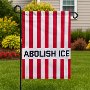 May include: A garden flag with alternating red and white vertical stripes. The words "ABOLISH ICE" are printed in bold, navy blue letters on a white rectangular banner across the center of the flag. The flag is displayed outdoors.