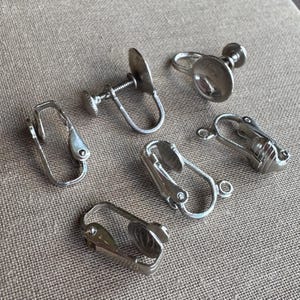 May include: A collection of silver-toned clip-on earring findings. The findings include various styles, such as screw-back and hinged clip designs. These components are used for creating or repairing non-pierced earrings.