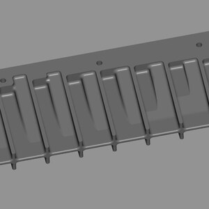 May include: A gray, rectangular mold with a series of vertical, rectangular indentations. The mold has a flat top and bottom with rounded edges. Two circular holes are present on each end of the mold.