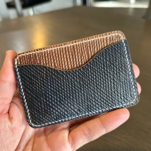 May include: A black and brown leather card holder with white stitching. The card holder has a textured surface and a curved edge.