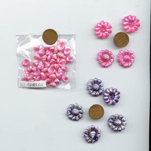 May include: A collection of pink and purple shell-shaped beads and embellishments. A clear plastic bag contains 50 pink shells. Several flower-shaped beads are also displayed, in shades of pink and purple. A penny is included for size reference.