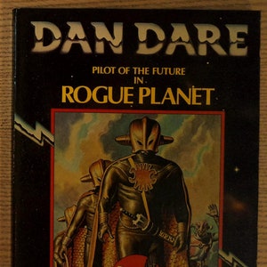 May include: A vintage paperback book cover featuring a sci-fi illustration of a futuristic warrior with a sword and a bird logo. The title is "Dan Dare, Pilot of the Future in Rogue Planet, Volume Two".