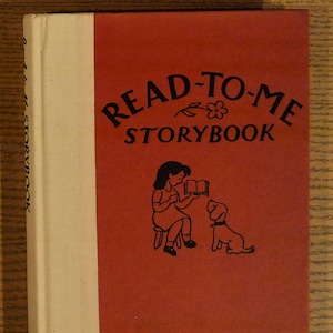May include: A vintage "Read-to-Me Storybook" with a red cover and a white spine. The cover features a black illustration of a girl reading to a dog. The title is in black script. The book is on a wooden surface.