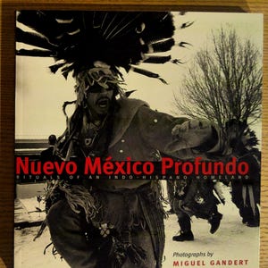 May include: A book cover with the title "Nuevo México Profundo" in red and white text. The cover features a black and white photograph of a person in ceremonial attire with a large headdress. The book is about rituals of an Indo-Hispano homeland.