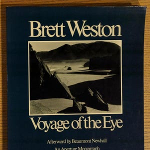 May include: A book cover with the title "Brett Weston" in white text above a black and white landscape photograph. The title "Voyage of the Eye" is below the photograph, with additional text at the bottom.