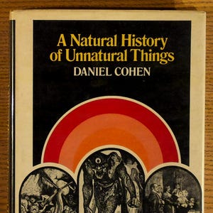 May include: A vintage book titled "A Natural History of Unnatural Things" by Daniel Cohen. The cover features a black background with a rainbow arch and illustrations of strange creatures and scenes.