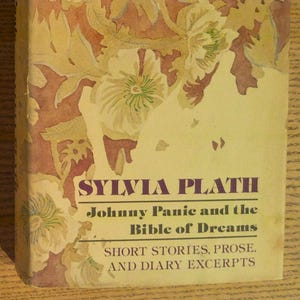 May include: A vintage book cover featuring the title "Sylvia Plath" in purple lettering. The book, "Johnny Panic and the Bible of Dreams," has a floral design in cream, yellow, and burgundy. The cover includes the text "Short Stories, Prose, and Diary Excerpts."