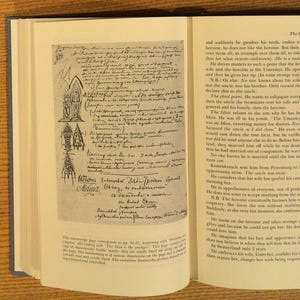 May include: An open book with text and a handwritten manuscript page. The manuscript features architectural sketches and Cyrillic script. The book's pages are aged, with text on the right page.