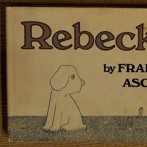 May include: A vintage book cover with the title "Rebecka" by FRANK ASCH. The cover features a line drawing of a dog sitting in a field of grass.