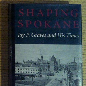 May include: A book titled "Shaping Spokane: Jay P. Graves and His Times" with a black cover and red lettering. The cover features a black and white photograph of a city street scene.