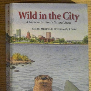 May include: A book cover with the title "Wild in the City: A Guide to Portland's Natural Areas" with a watercolor illustration of a river otter swimming in a river with a city skyline in the background.