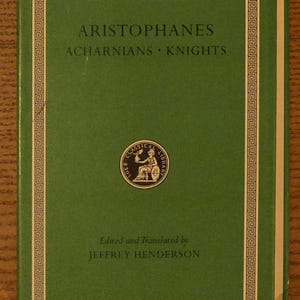 May include: A green hardcover book titled Loeb Classical Library Aristophanes Acharnians Knights edited and translated by Jeffrey Henderson. The cover features a gold Greek key border and a circular emblem depicting a seated figure.