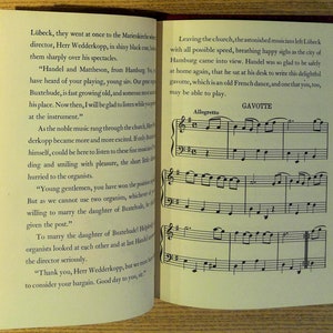May include: Open book with text and musical notation. The left page contains paragraphs of text, while the right page displays musical notes labeled "Gavotte" and "Allegretto". The book has a red cover.
