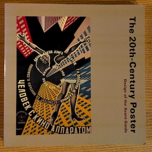 May include: A book cover featuring a vintage poster design. The poster has a central figure with arms outstretched, surrounded by text in a circular pattern. The color palette includes red, black, blue, and yellow. The title "The 20th-Century Poster" is displayed on the right.