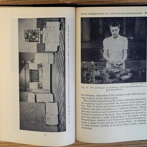 May include: A black and white photo of a woman preparing a salad in a kitchen. The kitchen has a white tiled floor and white cabinets. The woman is wearing a white shirt and a dark skirt. She is holding a bowl of salad with her left hand and a knife in her right hand. The photo is captioned "The techniques of preparing a tasty salad demonstrated in a permanent kitchen."