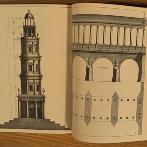 May include: Open book with architectural drawings. One page features a detailed illustration of a multi-tiered tower with classical architectural elements. The opposite page shows a section of a building with arches and columns. The drawings are in black and white.