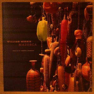 May include: A book cover titled William Morris Mazorca Objects of Common Ceremony. The cover features a dark background with a collection of hanging, textured, multi-colored sculptural objects resembling corn and gourds, and a glass vase.
