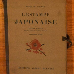 May include: A tan hardcover book titled L'ESTAMPE JAPONAISE by Gaston Migeon, published by Éditions Albert Morancé. The cover features a black spine, a red floral illustration, and text indicating it is from the Musée du Louvre, Première Série.